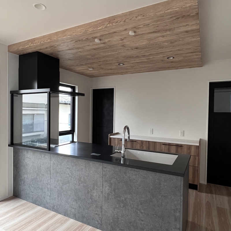 キッチンはブラック×グレーでまとめ、カップボードや折下げ天井は木目でまとめています。